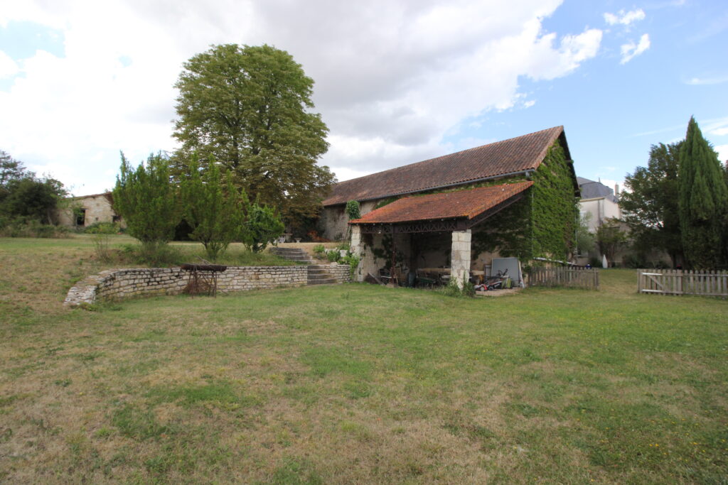 Ferme française traditionnelle avec grand jardin et ciel nuageux.